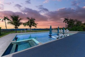 A home pool with lounge chairs and palm trees at sunset.